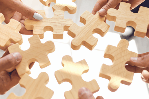 Mitarbeiter legen Puzzleteiele zusammen als Symbolbild für die Verwaltung mehrerer Unternehmen