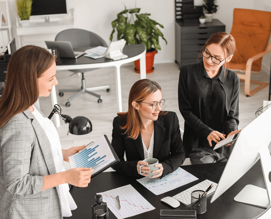 Drei Mitarbeiterinnen in der Buchhaltung diskutieren akutelle Finanzkennzahlen.